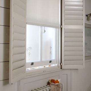 cream bathroom shutters on a window with a white blind
