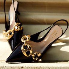 A pair of black Gucci heeled pumps with gold accents