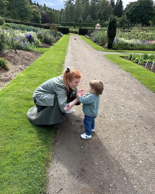 Sarah Ferguson wearing a green dress and jacket leaning down to talk to August Brooksbank on a garden path