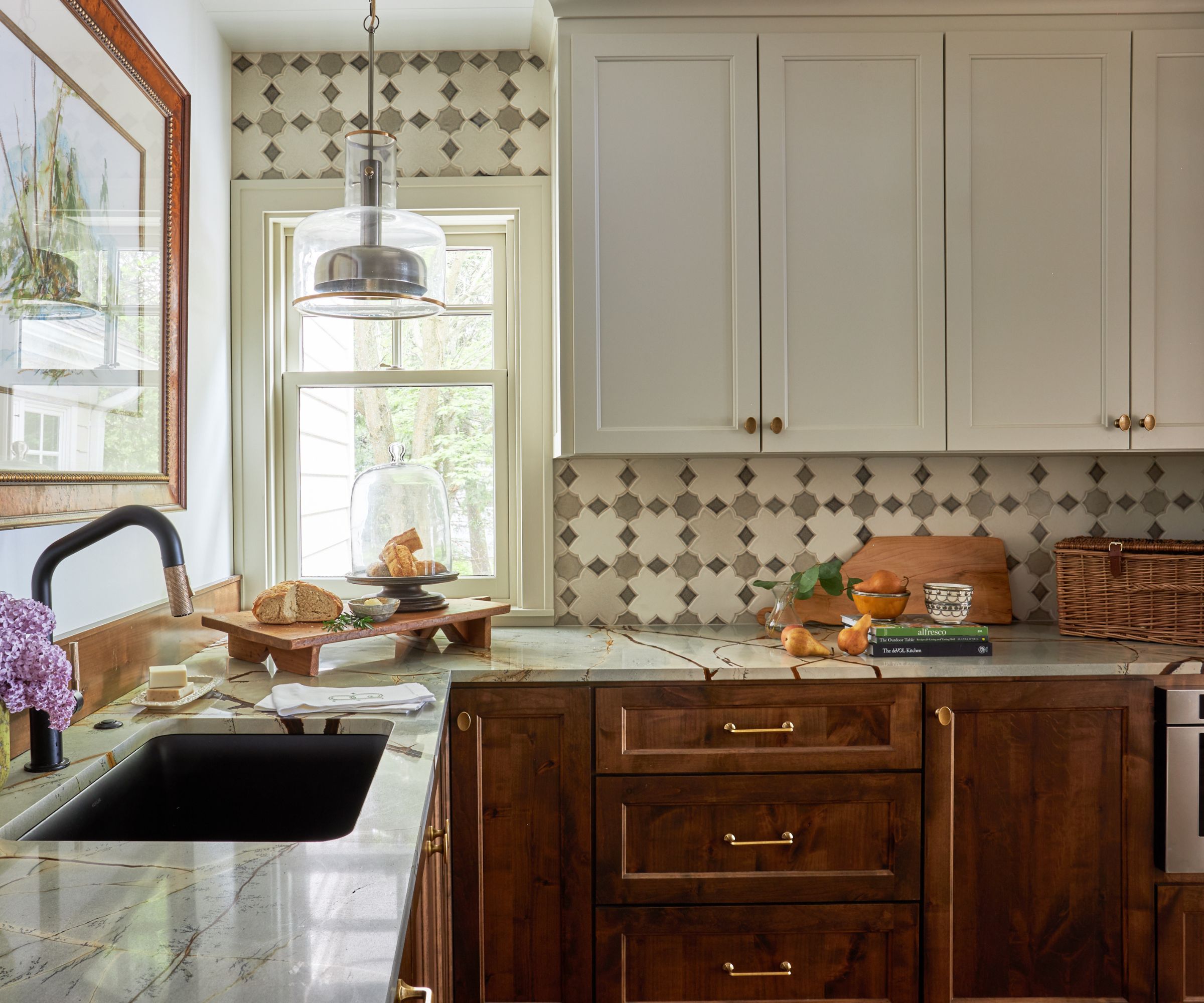 a cozy wooden and white two tone kitchen styled with marble countertops and a tiled backsplash