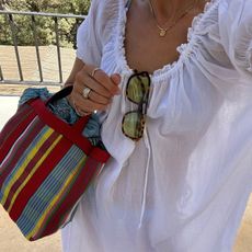 Lucy Williams wearing a white dress and carrying a striped market tote.