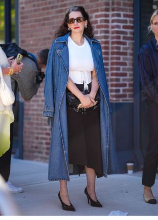 A woman in New York wearing a fitted white shirt with an asymmetrical black skirt and a long denim biker-collar coat.