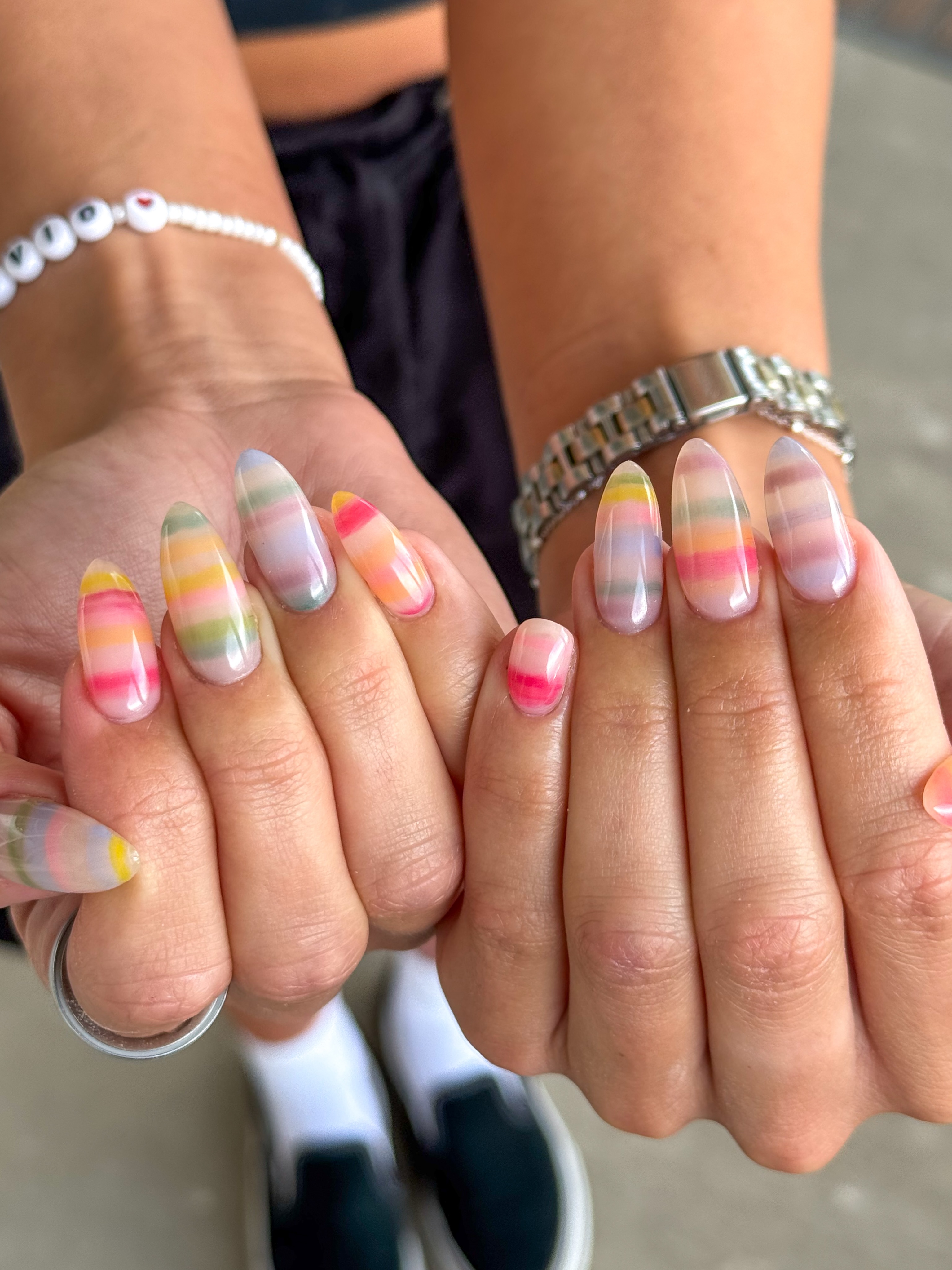 Sheer oval nails covered in blurred pastel stripes of pink, yellow, blue, and green