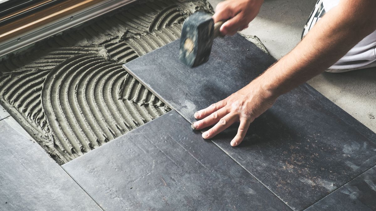 Man levelling slate grey floor tiles with rubber mallet