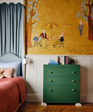 childrens room with a playful mural above neutral painted panelling and a green painted chest of drawers