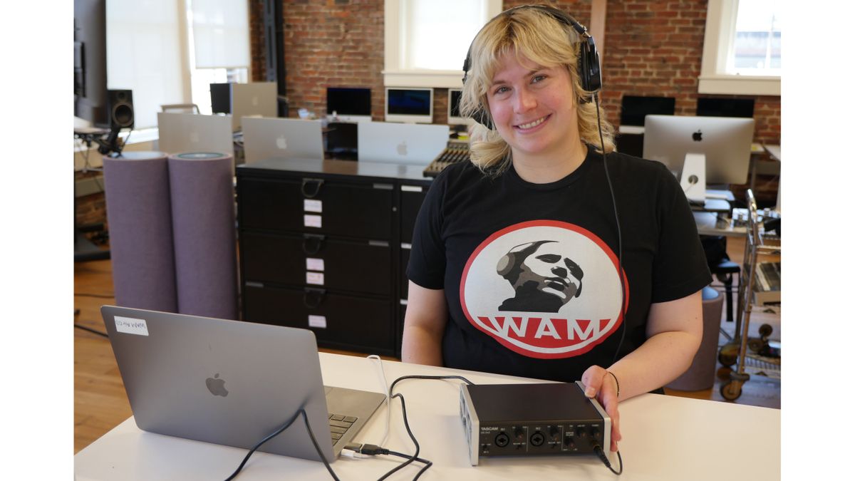 Arielle Flinkman of WAM smiling with headphones on a TASCAM equipment. 