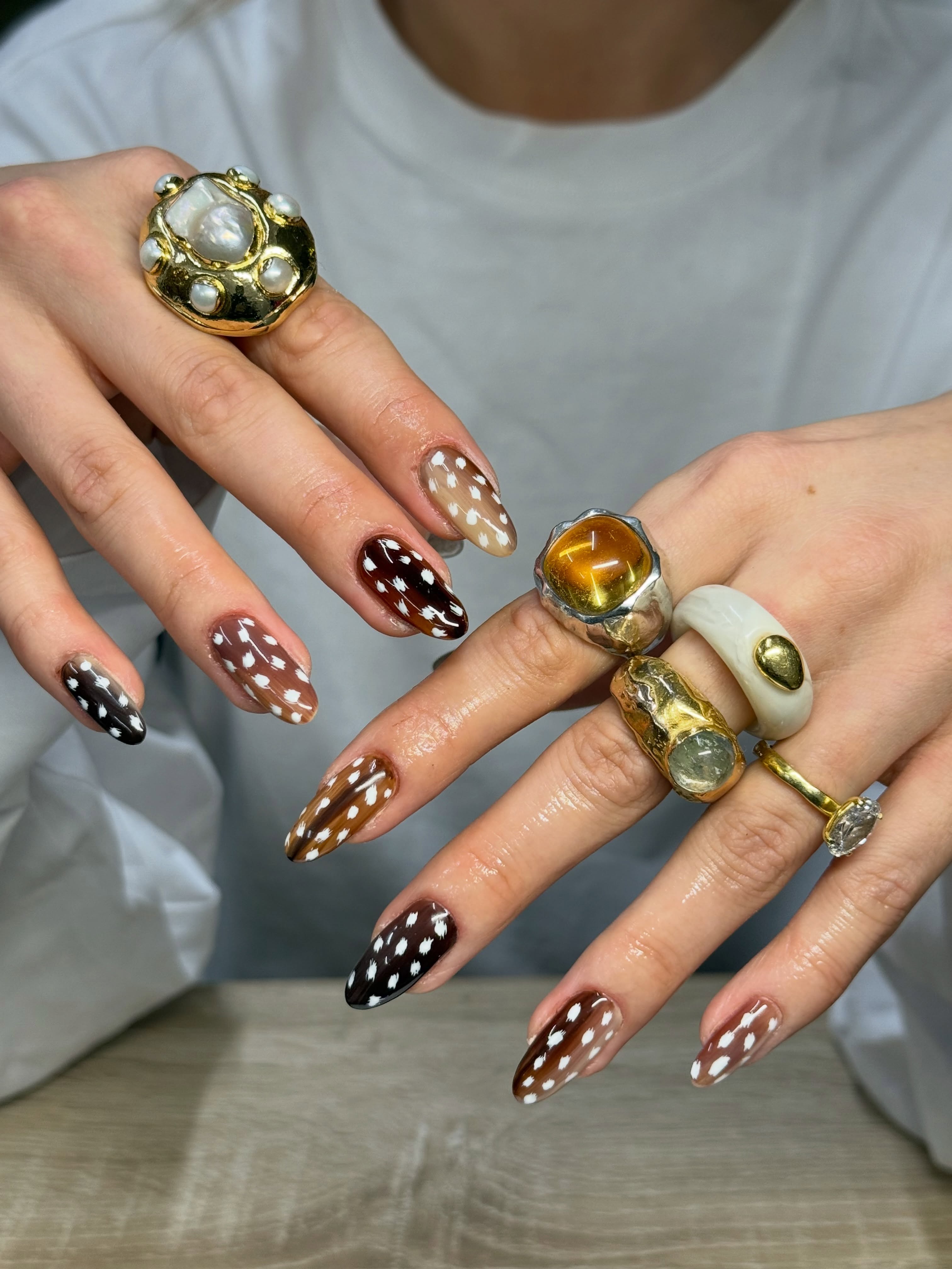 Almond nails in caramel, chestnut and dark brown shades covered with irregular white fawn spots