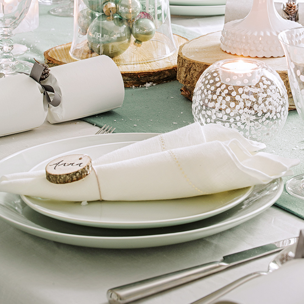 white Christmas napkin rolled to a point on white dinnerware with slices of tree stump as decoration