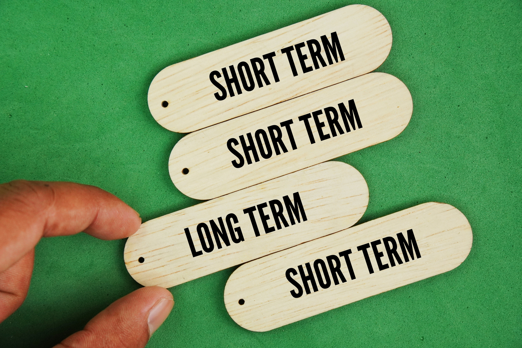 Hand and stick with two choices of words long term and short term. Long-term planning refers to setting goals and outlining strategies that span several years into the future