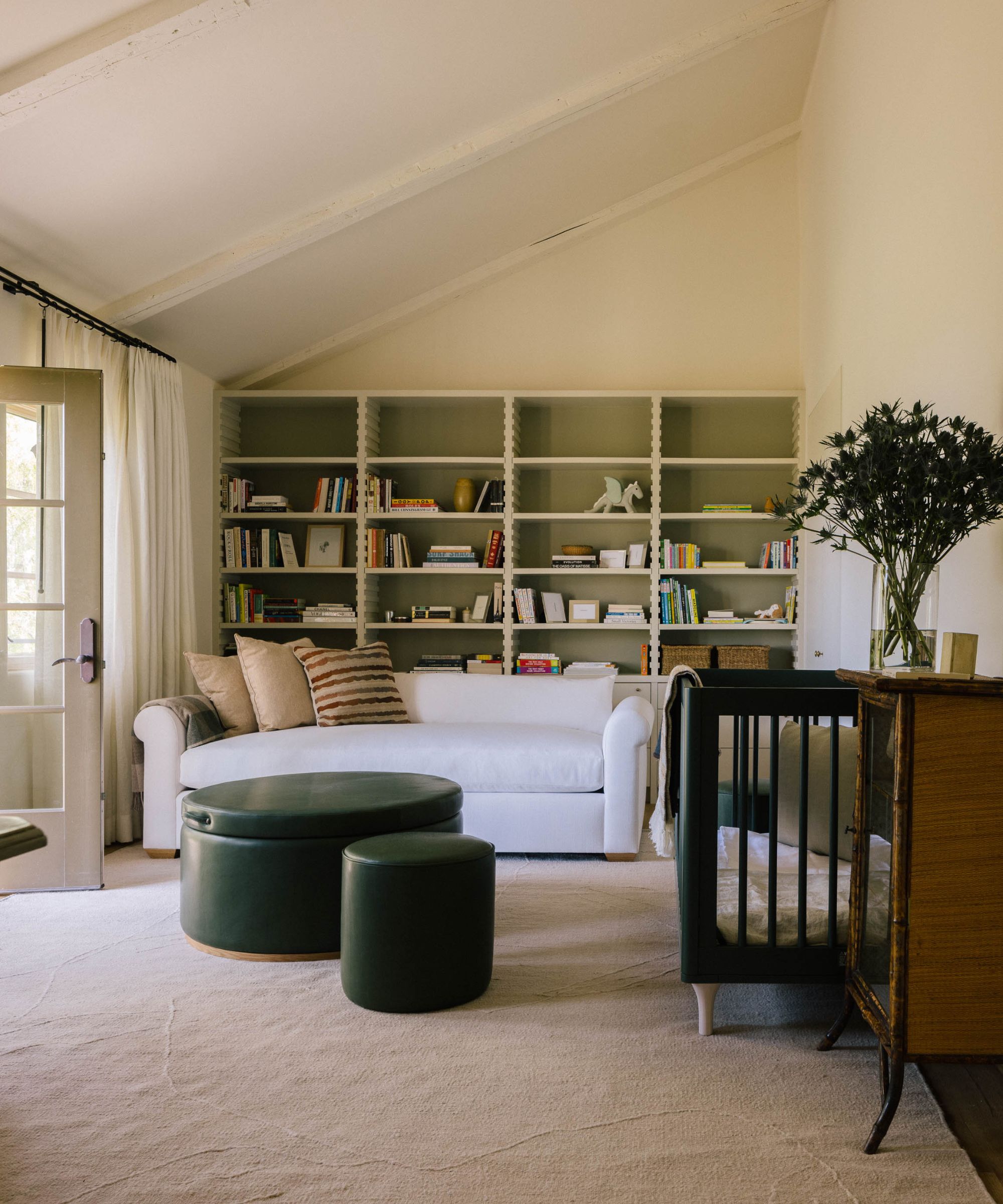 a neutral nursery bedroom with sloped ceiling, bookcases, a white sofa, black crib and large plush crib