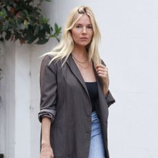Sienna Miller wears a gray blazer with high waisted jeans.