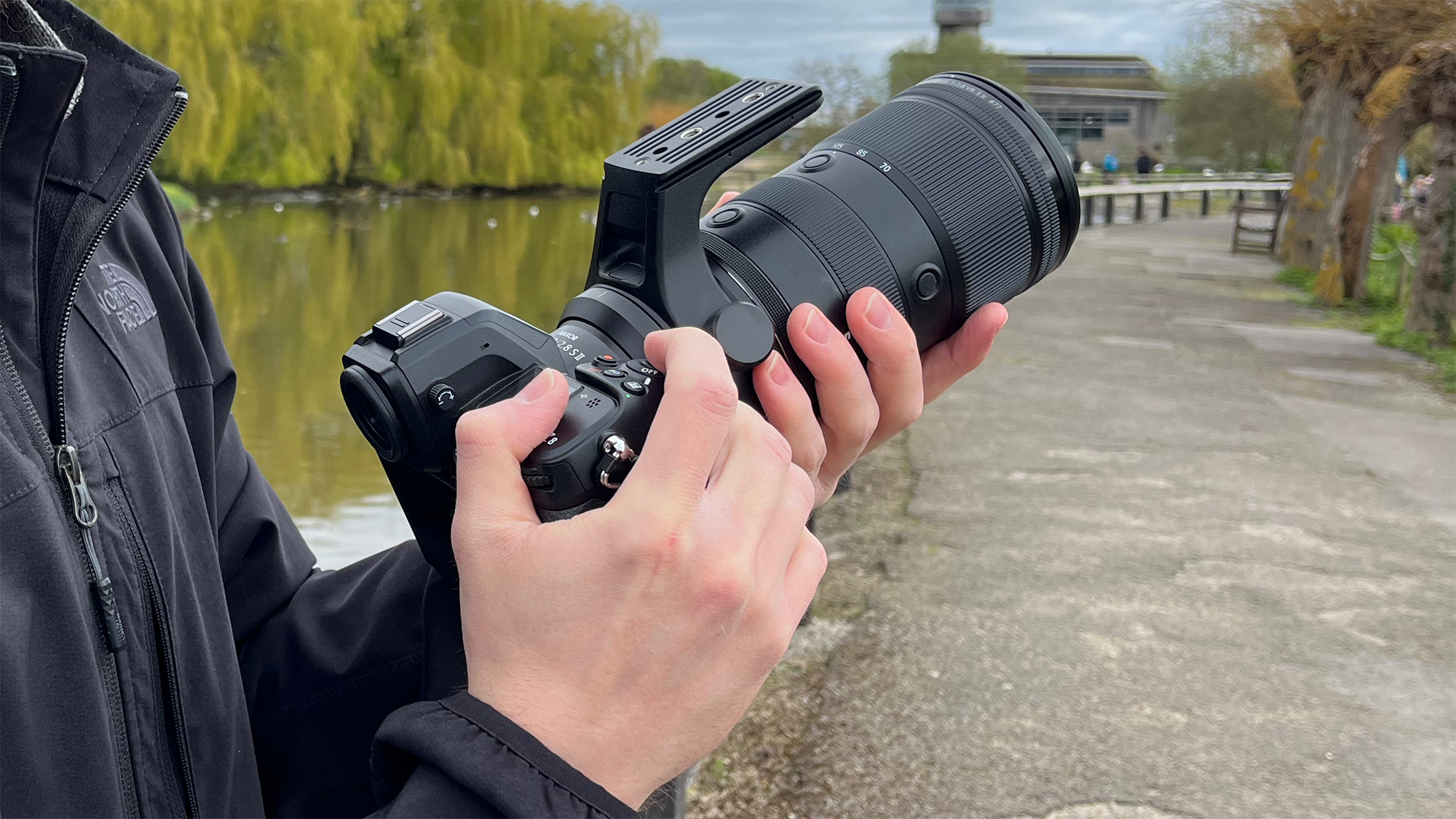 Mike Harris holding Nikon Z 70-200mm f/2.8 VR S II by a lake with vegetation and trees in the background 