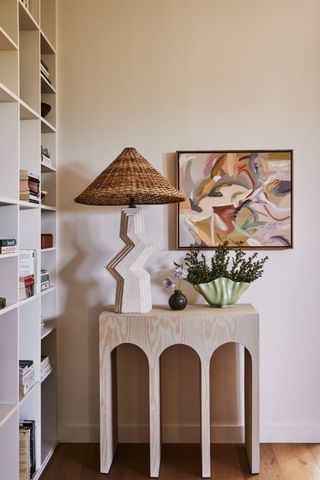 console table in hallway with lamp, vase and art, next to bookshelf