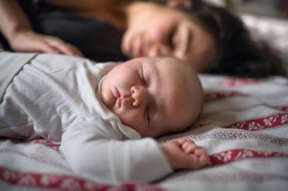 Mother with newborn baby indoors at home, co-sleeping on bed.