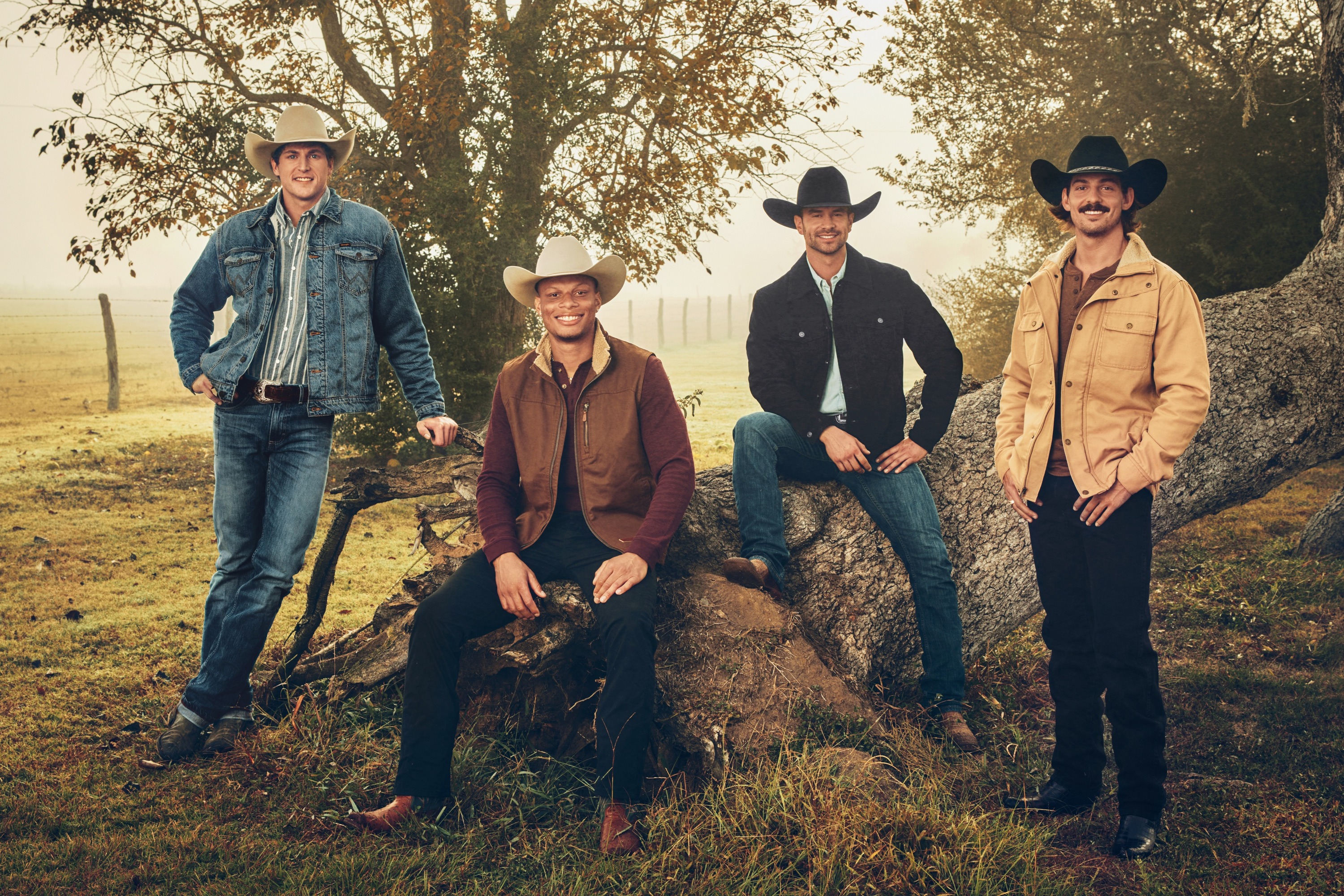 four cowboys in jackets jeans and cowboy hats sit by a tree in a promo shot for the show farmer wants a wife