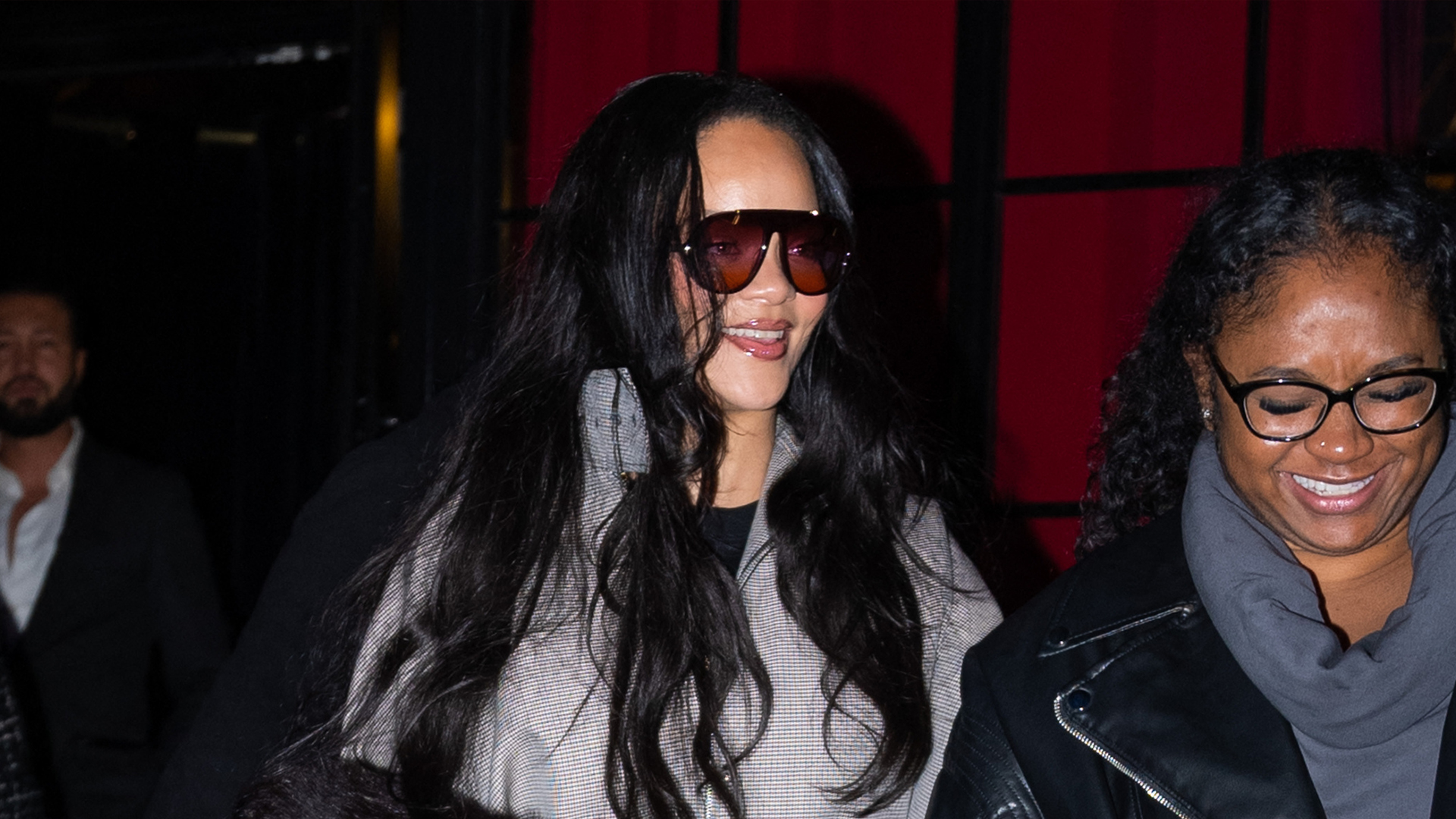 Rihanna wearing black sunglasses, plaid funnel neck jacket, slit leggings, and red lace up pumps.