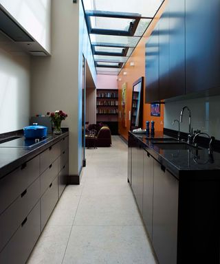 Long galley kitchen with dark units and orange wall beyond