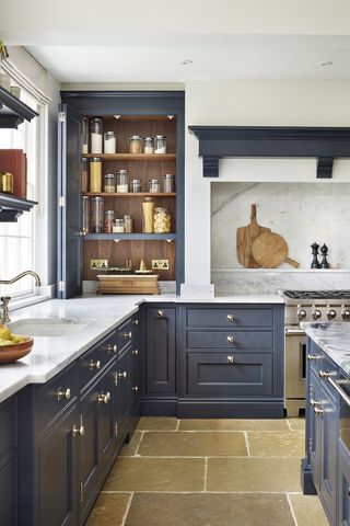 A bright kitchen with dark blue cabinets and pantry door open