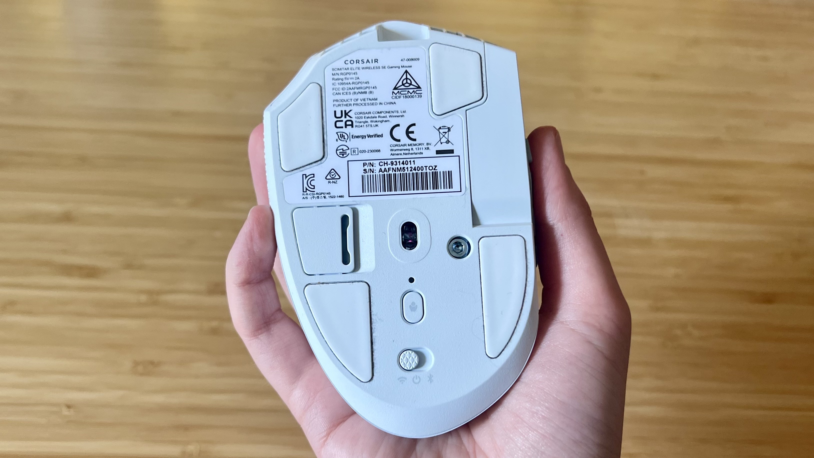 Underside of Corsair Scimitar Elite Wireless SE gaming mouse showing sensor and PTFE feet, held in reviewer's hand