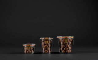 Milla Chocolates hazelnut coffee truffles in 3 different sizes of clear containers photographed against a black background