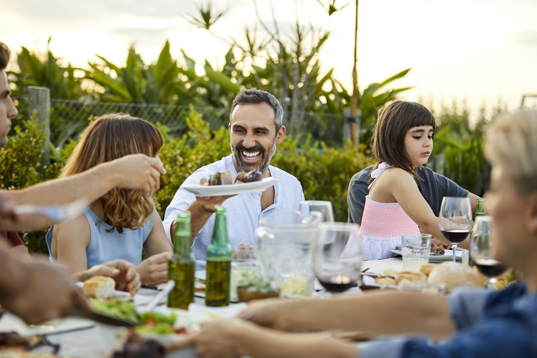 Happy friends having food at table in backyard. Males and females are celebrating Asado. They are enjoying weekend together.