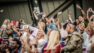 A group of fans taking a selfie with a smartphone while watching a match in a stadium