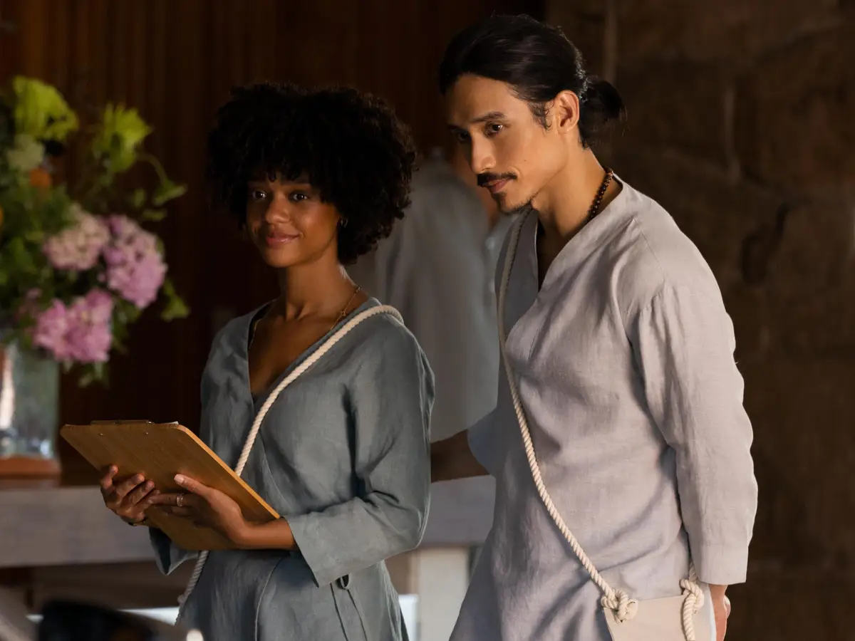 delilah and yao wear their grey work uniforms and hold a clipboard in nine perfect strangers