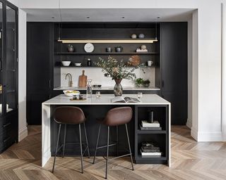 Breakfast bar ideas incorporated into a white marble kitchen island in a black kitchen scheme with wooden herringbone flooring.