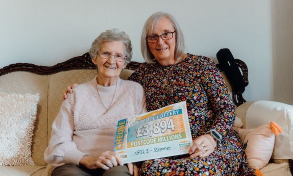 Postcode Lottery winners holding a cheque and smiling