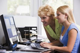 A mother and daughter look at a computer screen together