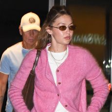 Gigi Hadid wearing a pink cardigan, white T-shirt, jeans, and loafers with socks at JFK
