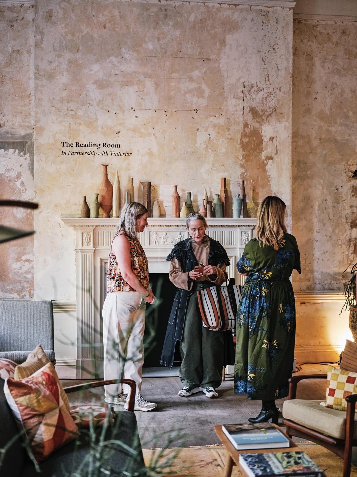 A series of installation shots from a show hosted inside a historical building with unfinished walls and tall ceilings captures the soft atmosphere inside it, punctuated by floating artworks, crafty furniture and accessories, and people chatting or performing.