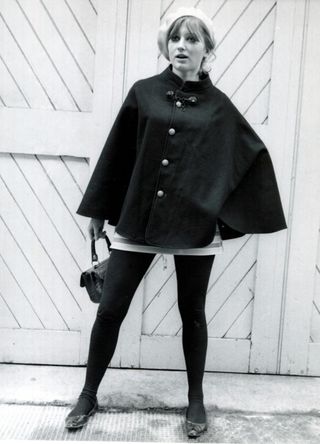 Women's Fashion 1966: Model wearing a black cape, white beret and white striped mini skirt with black tights and shoes.