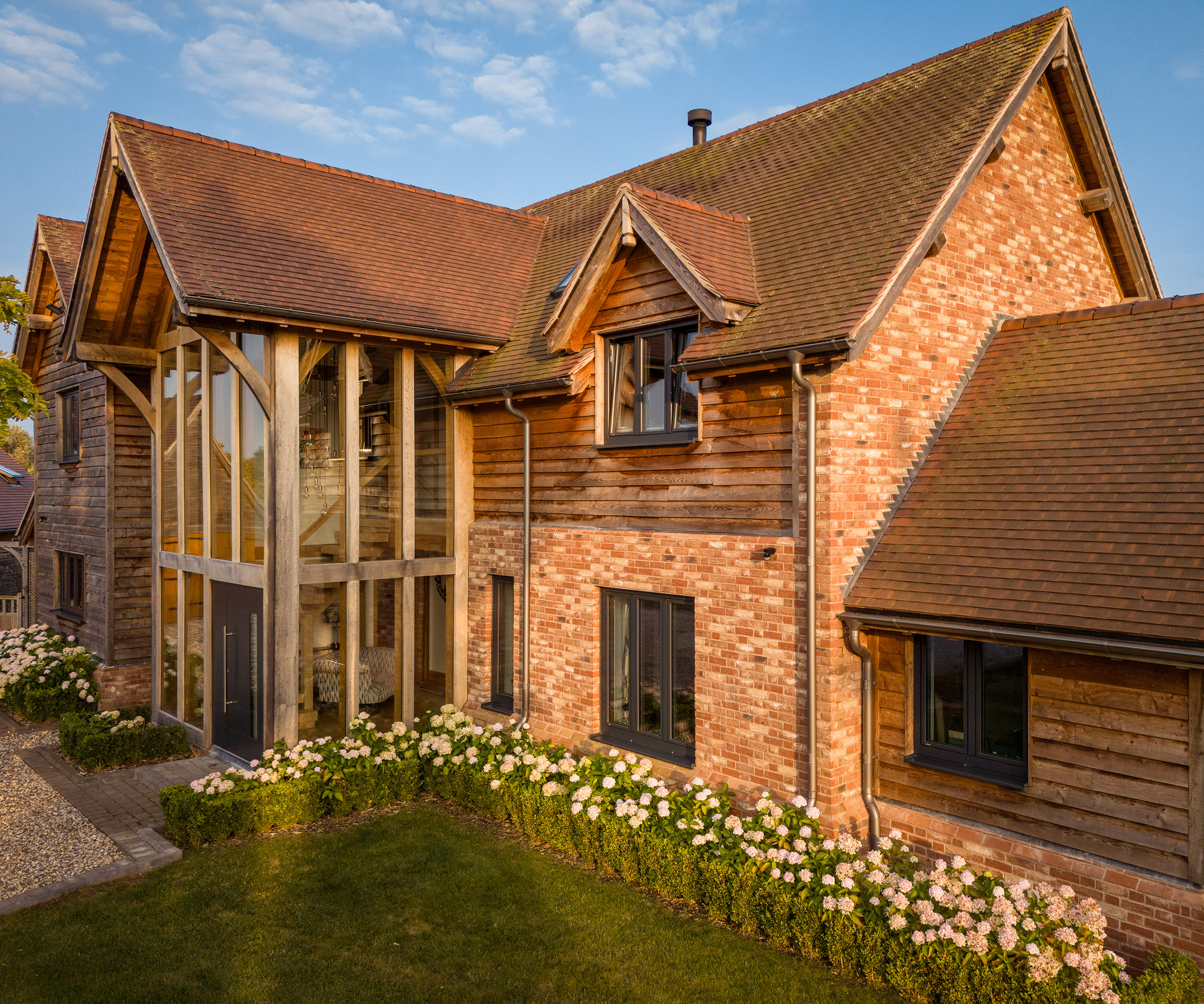 A large red brick and timber clad home with double height glazing and a pitched roof