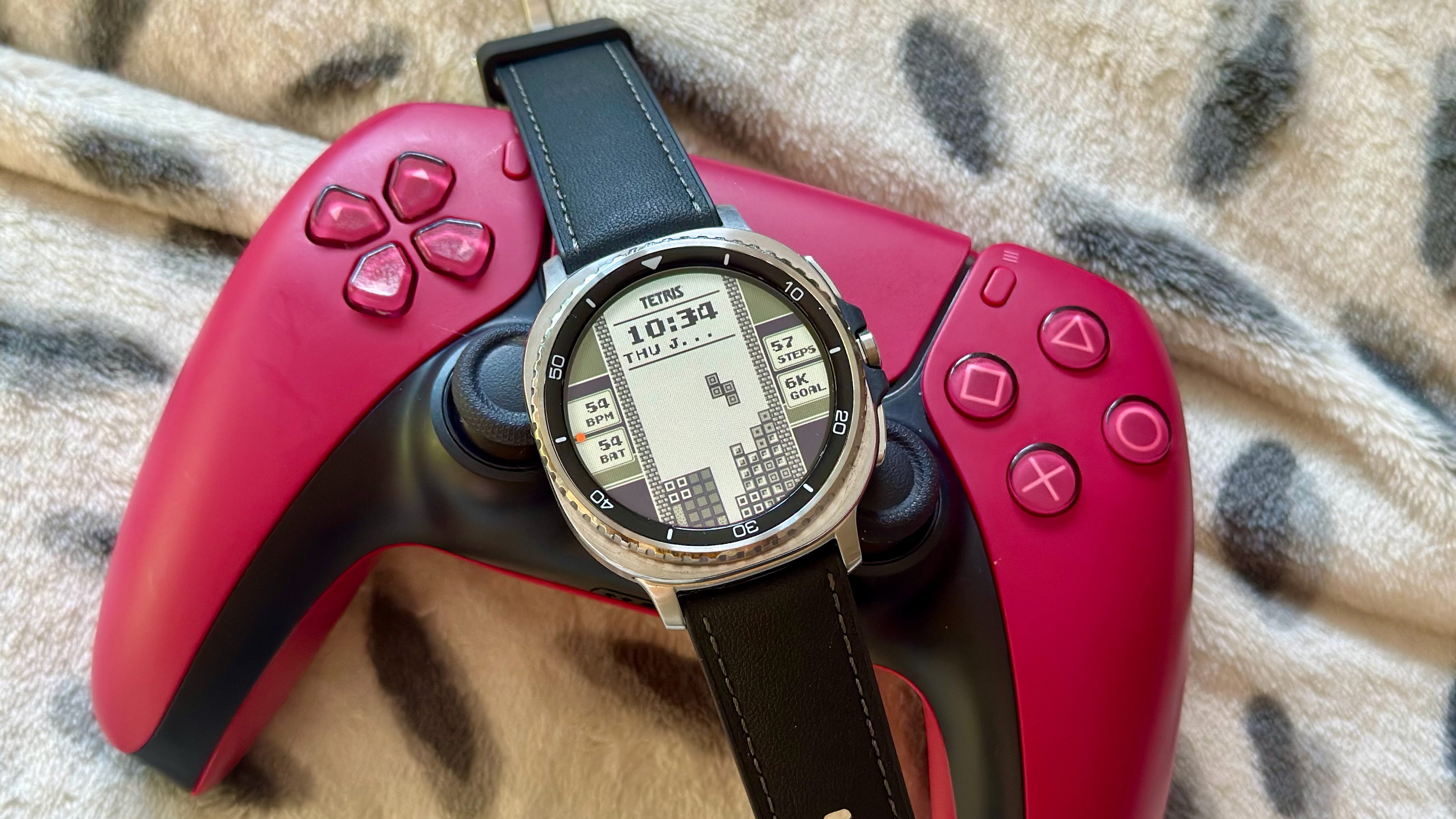 The Samsung Galaxy Watch 8 Classic resting on a gaming controller, showing a custom Facer watch face of a game of Tetris.