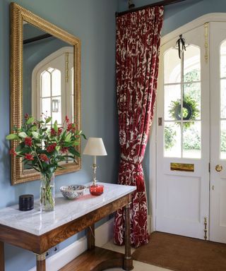 Narrow hallway ideas with blue walls, red patterned drapes and a mirror.