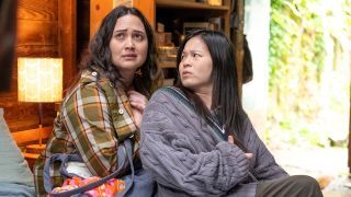 Lily Gladstone and Kelly Marie Tran looking concerned while sitting on a bed in The Wedding Banquet