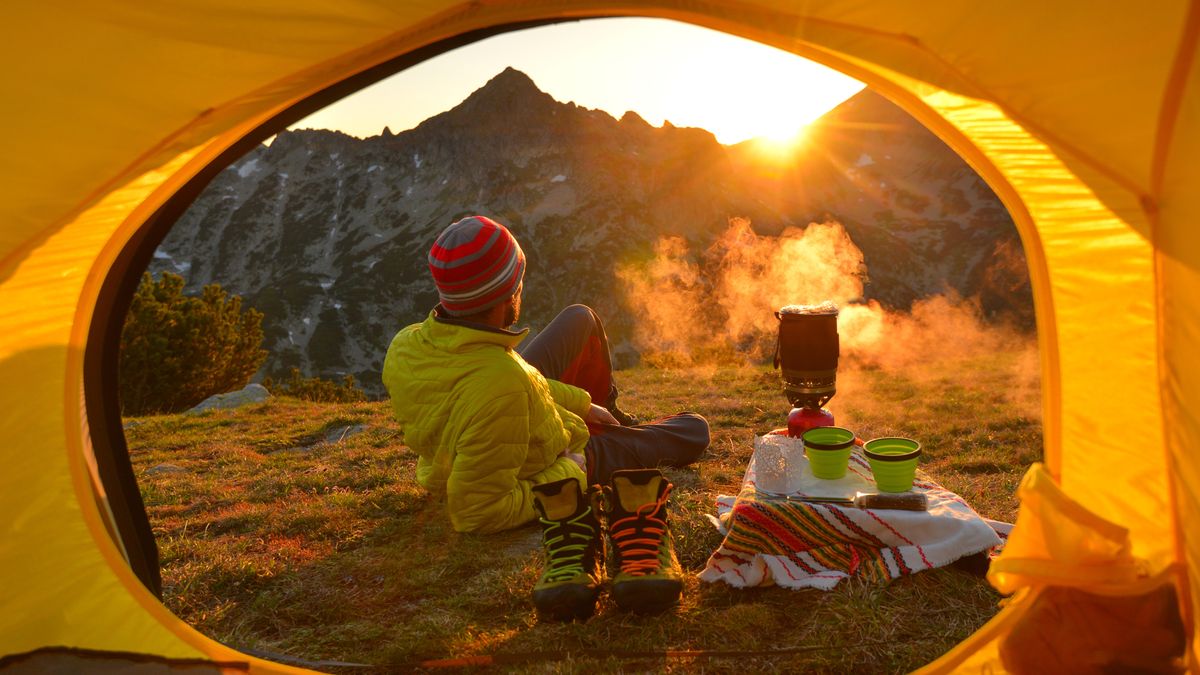 A man cooking on a stove outside his tent at sunset