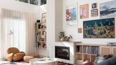 A living room with a tiled fireplace, a sofa and pouf set, a floor lamp, a gallery wall of framed art, open vinyl storage and wall-mounted shelving
