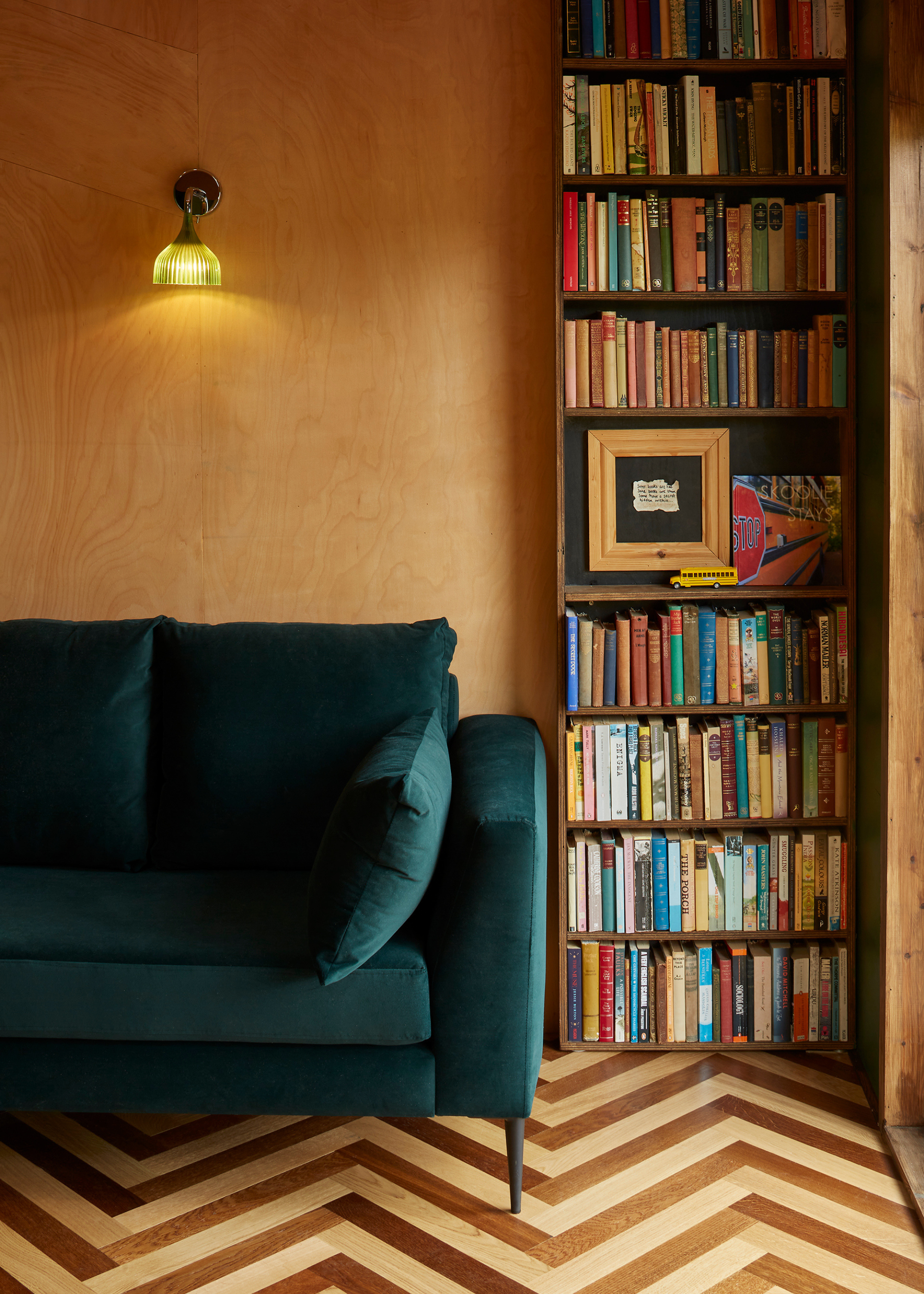 a mid century inspired room with wooden walls and contrast wood parquet flooring and a green velvet sofa