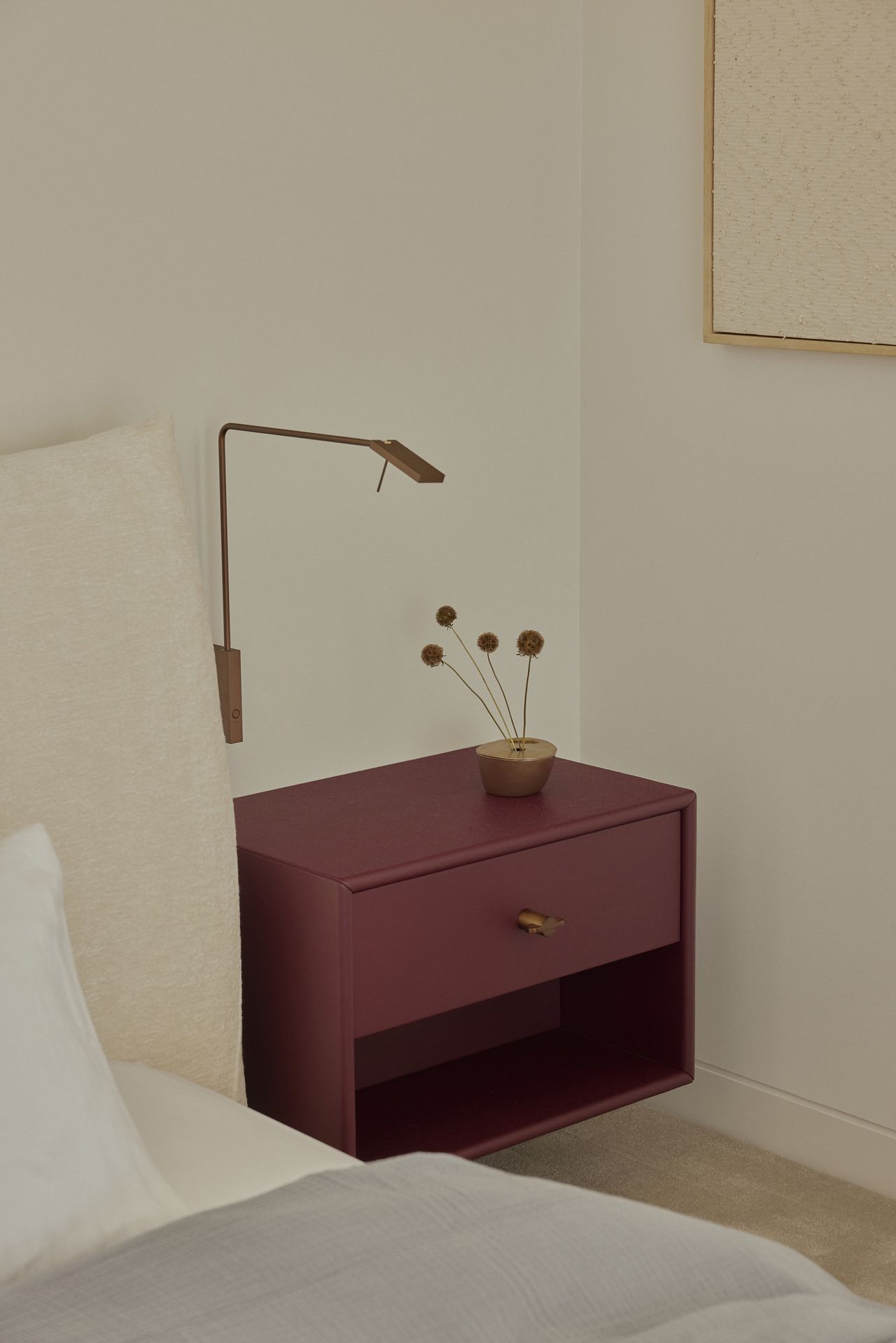 modern beige bedroom with burgundy bedside table with brass wall sconce