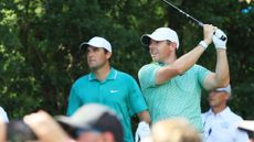 Rory McIlroy hits a tee shot as Scottie Scheffler watches on