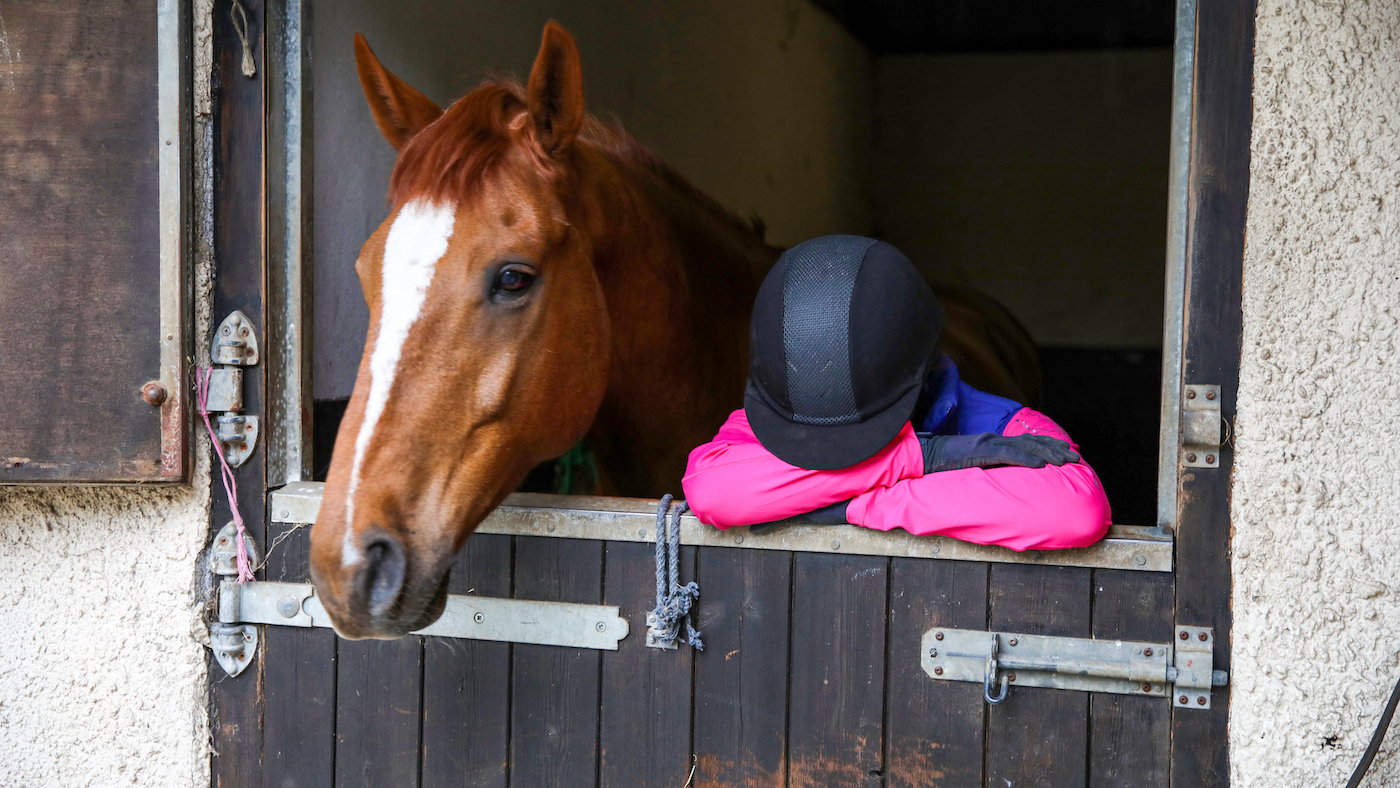 Sad rider standing by horse in stable.