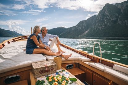 A senior couple relaxes on a boat while staring out at the water and mountains. 