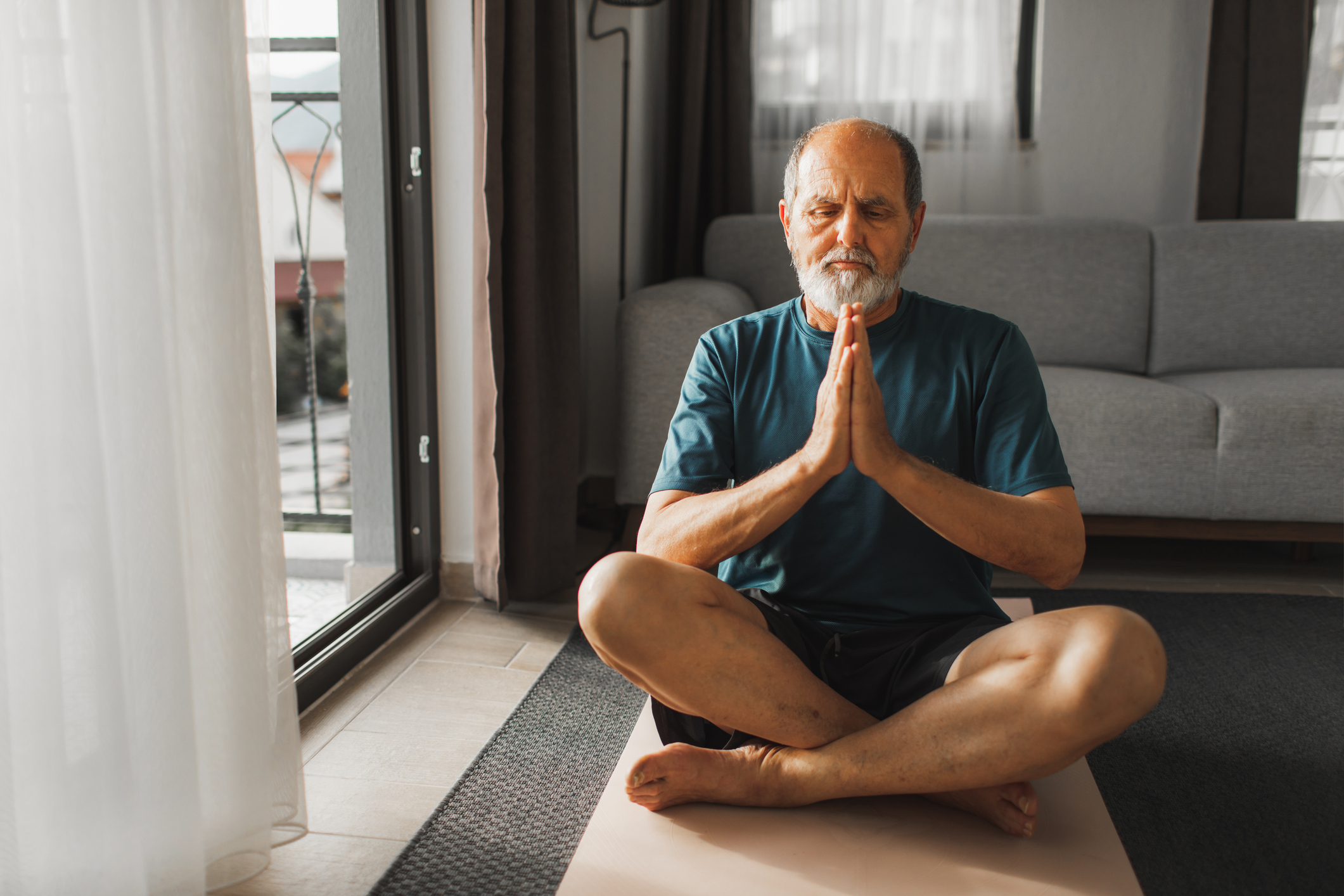 An older man with his eyes closed sitting on the ground and meditating in the sunlight.