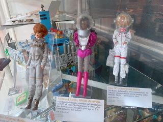 a trio of dolls behind glass in astronaut suits
