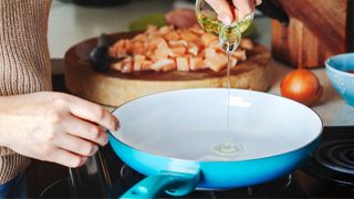Woman pouring olive oil into a blue non-stick ceramic pan