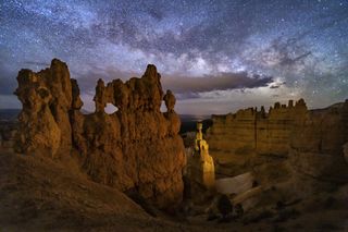 A hoodoo with small windows and Thor's Hammer against a night sky with clouds and the Milky Way below Sunset Point in Bryce Canyon National Park, Utah.