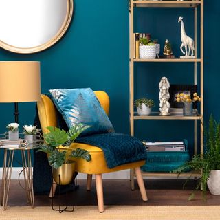 Yellow armchair with blue cushion and throw, with blue wall, mirror and shelf