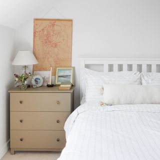 country cottage bedroom with neutral bedding, white bedframe and a small bedside chest of drawers with bedside lamp